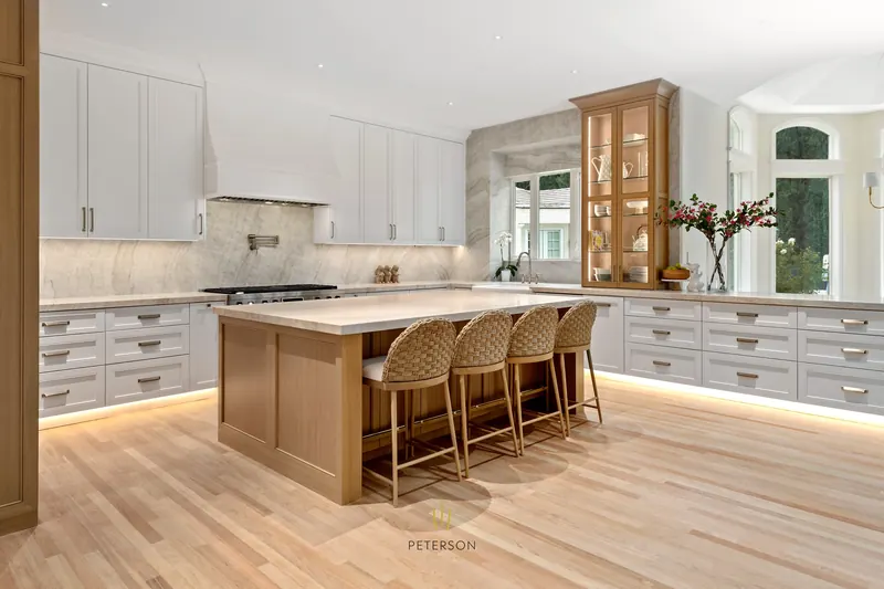 Wide view: light-wood island, white perimeter cabinets, glass display hutch