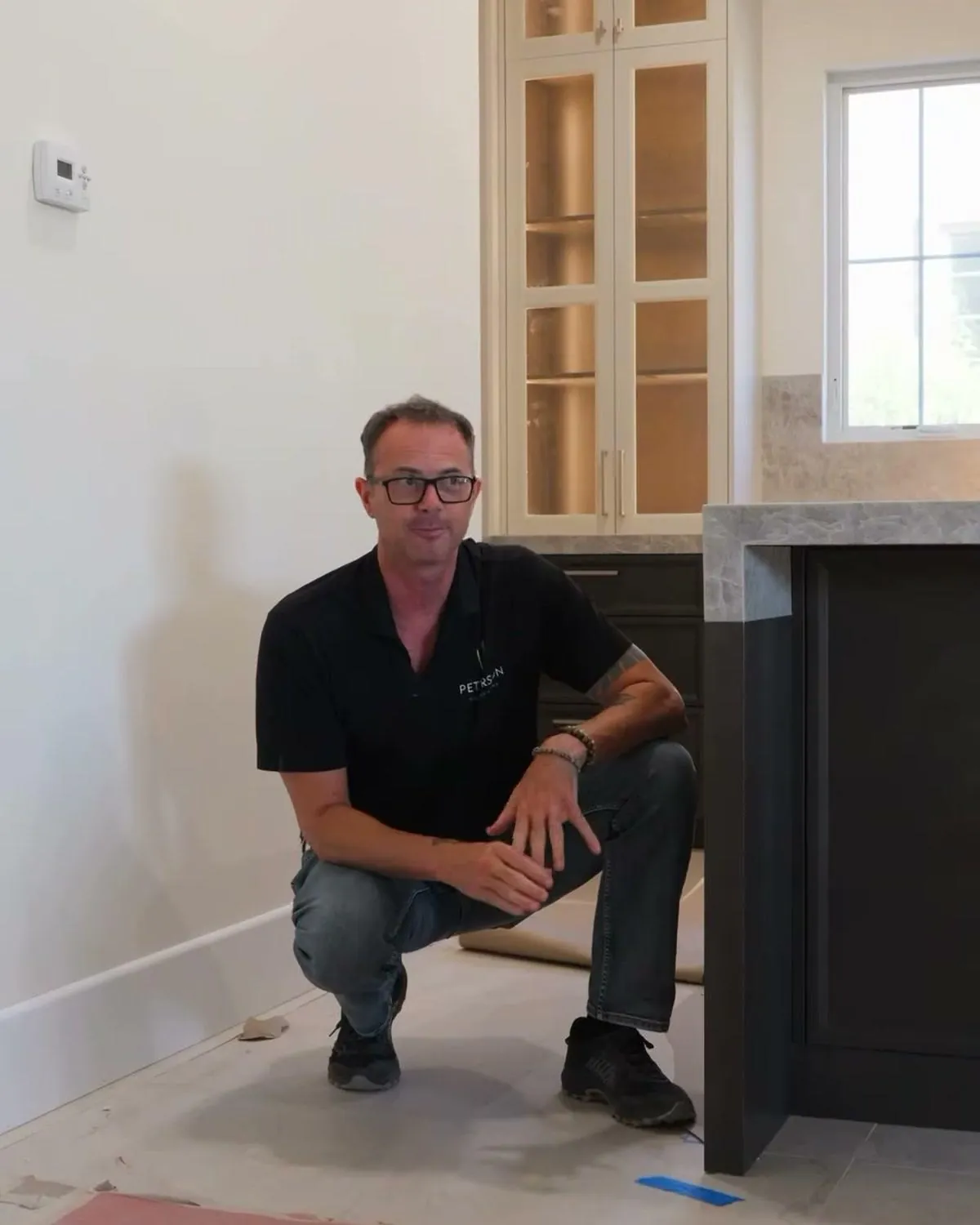 Dave Peterson crouched beside a custom cabinet island explaining flooring or cabinets first
